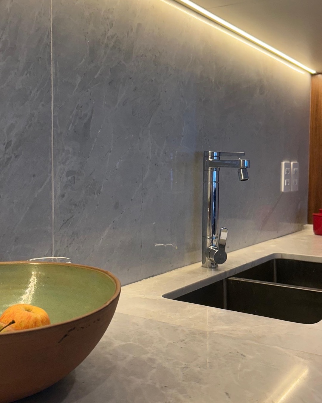 Detalhe de bancada de cozinha em pedra clara com cuba embutida e iluminação linear