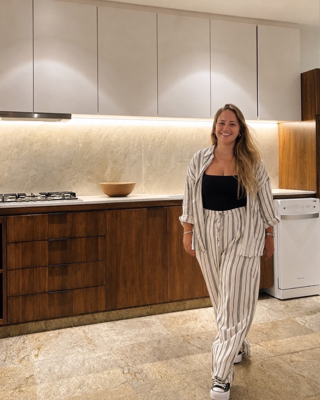 Tatiana, fundadora e CEO da TG Arquitetura & Reformas, em cozinha com marcenaria em madeira, bancada em pedra clara e iluminação embutida